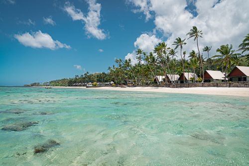 Beautiful white sandy beach and turquoise clean waters under blue summer sky. Vacation Paradise Fiji. Coast along Korotogo, South Coast, Western Division, Fiji, Oceania.