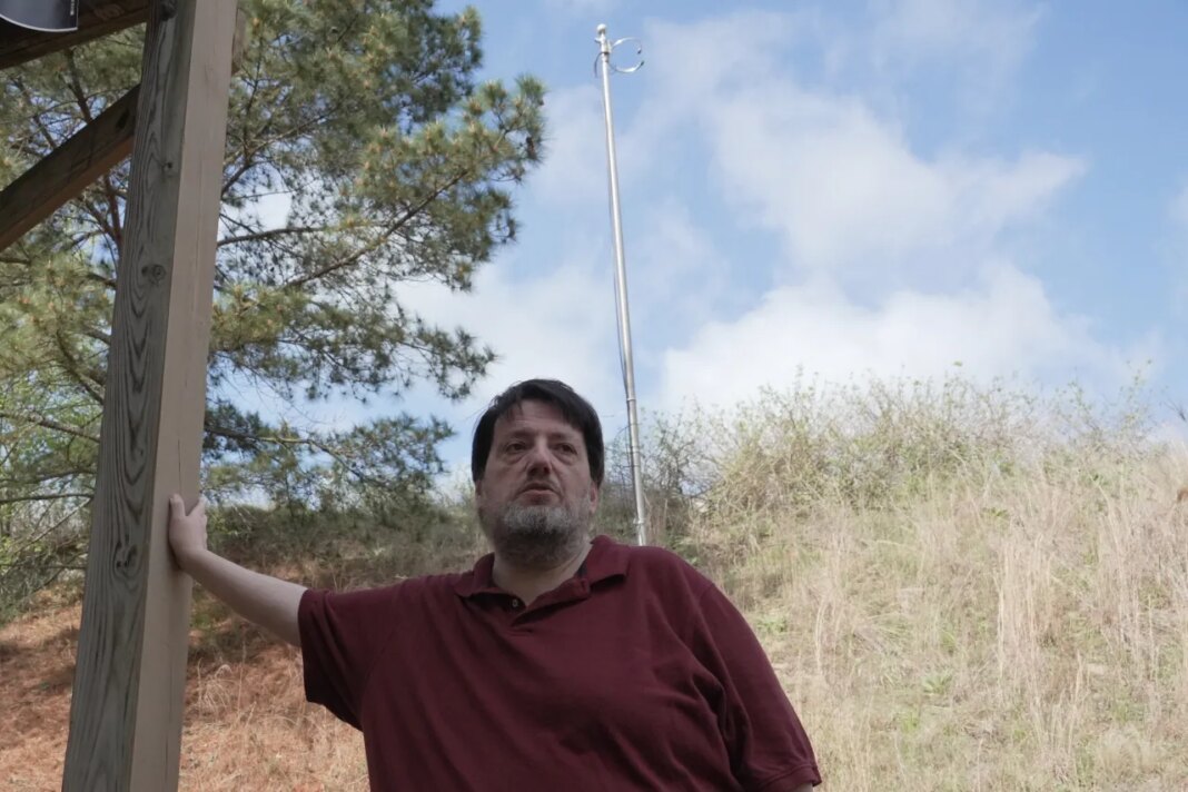 D.P. McIntire leans against a deck beneath the WKRP radio antenna in the backyard of his home in Raleigh, N.C., on Thursday, April 2, 2026. (AP Photo/Allen G. Breed)