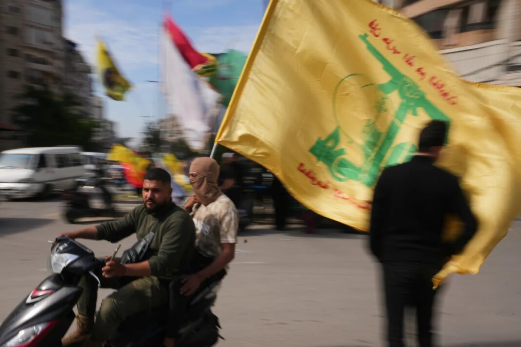 Men ride a scooter while waving a Hezbollah flag during a small gathering in Dahiyeh, Beirut