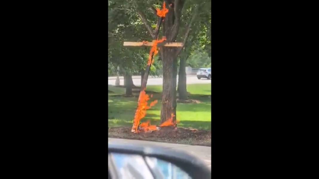 This framegrab from a video taken by motorist Keinika Carlton shows a wooden cross engulfed in bright orange flames as it leans against a tree in Grant Park in Chicago on Tuesday, July 9, 2026. (Keinika Carlton via AP)