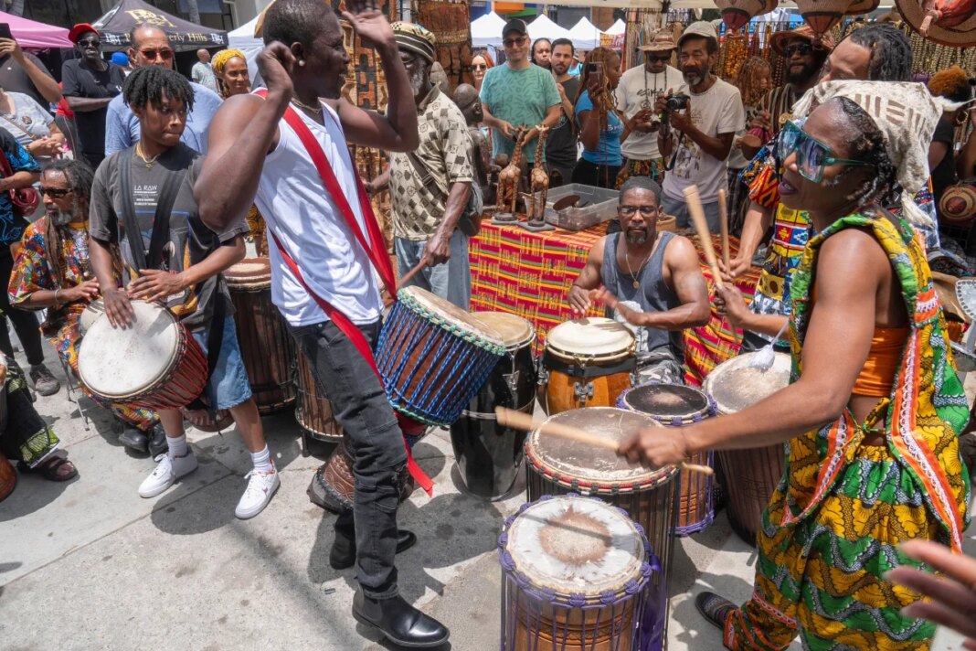 FILE - Drummers form a circle around Sika Dwimfo, better known as the, "Godfather of Leimert Park," during the neighborhood