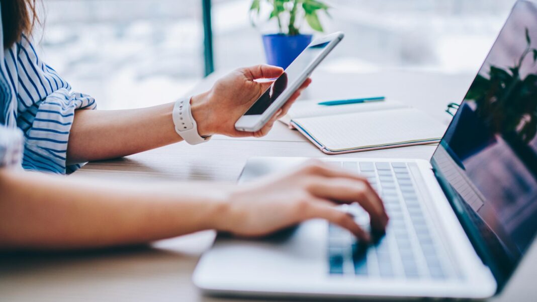 Cropped image of female holding smartphone getting message with confirmation making transaction on laptop computer,woman using mobile phone app